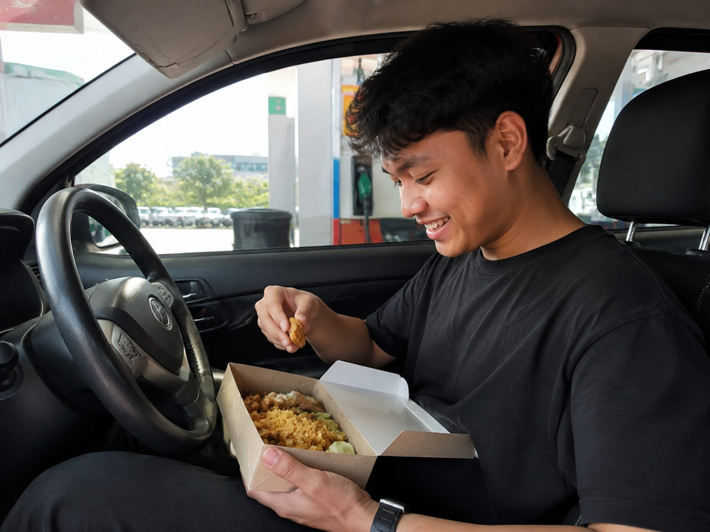 Someone happily eating a Foodplus meal in their car at the station